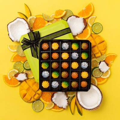 25 count box of chocolate on yellow background. Tropical fruits surrounding box of chocolate. 